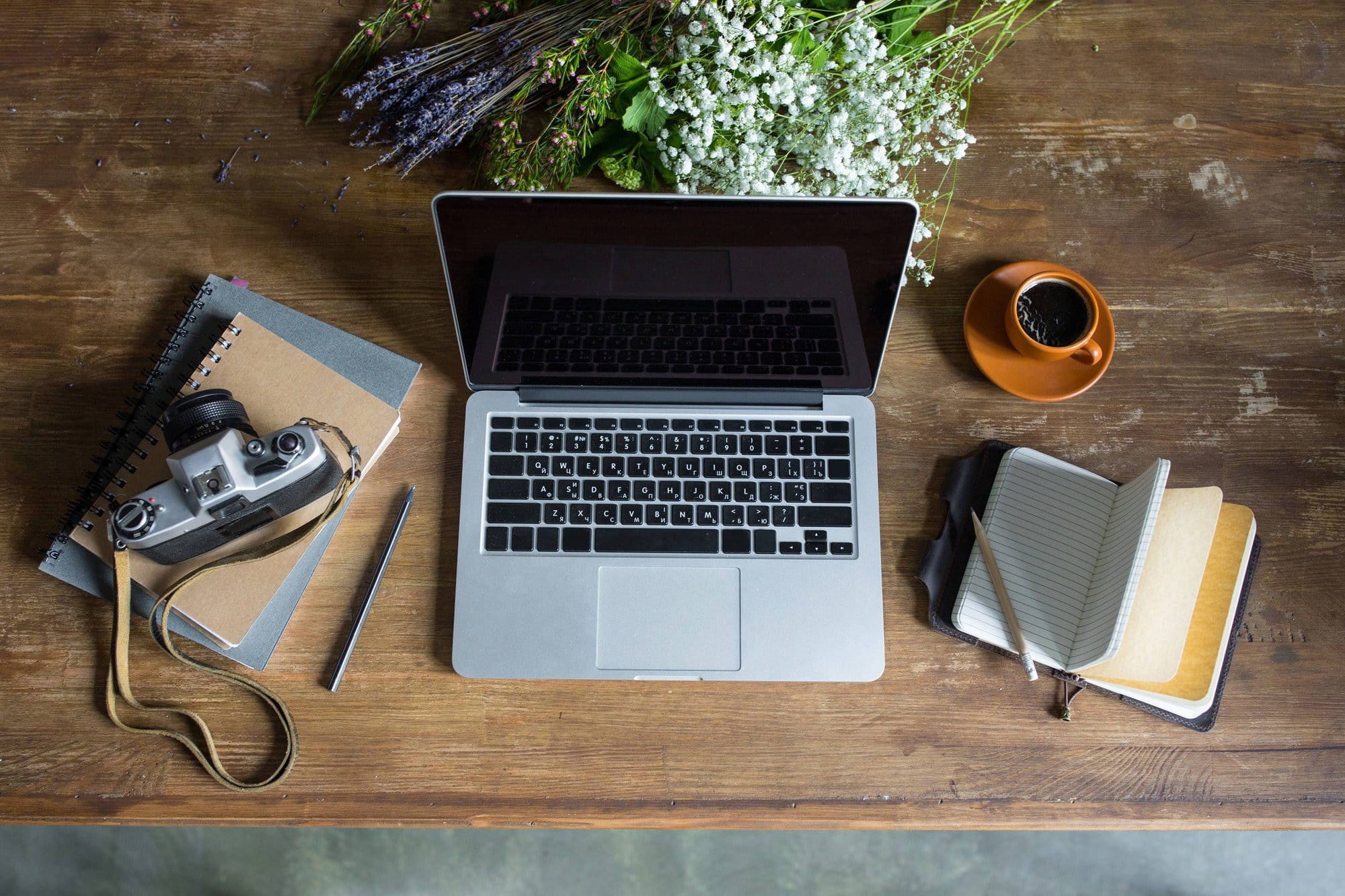 top view of laptop, diaries, vintage photo camera and cup of coffee on wooden tabletop- freelance writing jobs